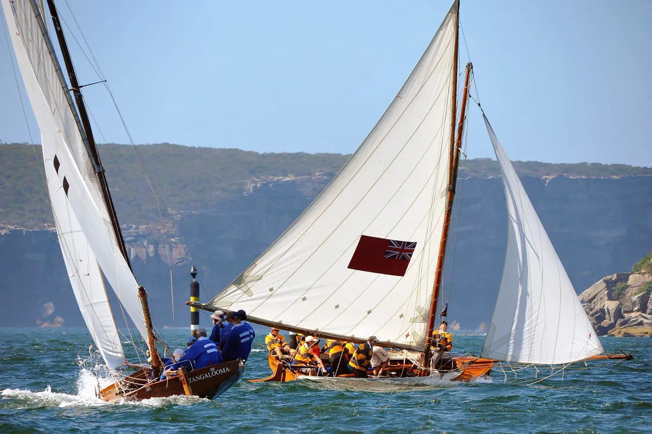 Tangalooma and Britannia crossing tacks beneath the North Head cliffs, crews in blue and mustard
